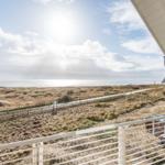Blick von Balkon auf Strand und Meer unter blauem Himmel mit weißen Wolken.