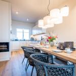 Essbereich mit Holztisch und Stühlen, Küchenbereich im Hintergrund, modernes Design mit integriertem Kamin.