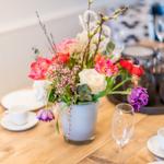 Holztisch mit Blumenarrangement, Tassen und Gläsern. Kerzenhalter auf dunklem Tablett.