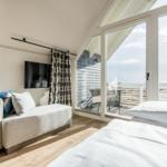 Schlafzimmer mit Blick auf die See und Balkon. Bett, Sofa und Fernseher sichtbar.