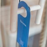 Ein blaues Schild mit der Aufschrift Sauna hängt an einem Holzgriff.
