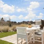 Terrasse mit weißem Tisch und Stühlen, Blick auf Gras und Häuser.