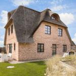 Rotes Backsteinhaus mit Strohdach und Gartenbereich mit weißem Mobiliar.