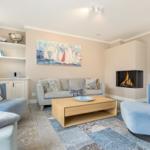 Wohnzimmer mit Sofa, zwei Sesseln, Kamin und Wandbild mit Segelbooten.