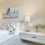 Schlafzimmer mit Bett, Nachttisch und Wandbild mit Segelbooten.