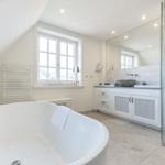 Dusche, Badewanne und Waschbecken in einem hellen Badezimmer mit Fenster und Spiegel.
