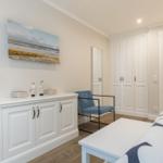 Schlafzimmer mit weißem Schrank, blauer Sitzgelegenheit und Wandbild