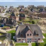 Dorfhaus mit Strohdach und Garten, Blick auf Meer und umliegende Häuser.