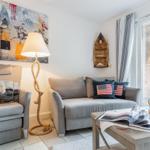 Wohnzimmer mit Sofa, Sessel und Tisch. An der Wand hängt ein Bild und eine hölzerne Bootswand. 