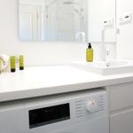 Waschmaschine unter Waschtisch mit Spiegel und Dusche im Hintergrund.
