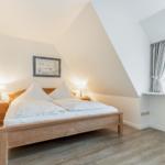 Schlafzimmer mit Dachschrägen, Holzbett und Fenster mit Vorhängen.