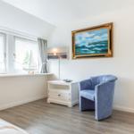 Zimmer mit blauem Sessel, Wandbild und Fenster mit Segelbootmodell.