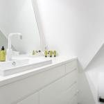 Weiße Dusche mit modernem Waschbecken und Spiegel. Dachboden-ähnliche Decke.