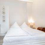 Schlafzimmer mit weißem Bett, Nachttisch und Wanddekoration.