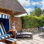Terrasse mit Strandkorb, Tisch und Stühlen. Hinterhof mit Hecke und Steinmauer.
