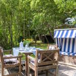 Garten mit Tisch, Stühlen und Strandkorb unter Bäumen.