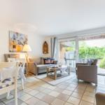 Wohn- und Essbereich mit Terrasse, Sofa, Stühlen und Tisch. Wandbild und Gardinen sichtbar.