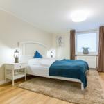 Bedroom with white bed, blue blanket, desk and TV.