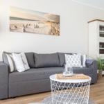 Living room with gray sofa, white table, and beach wall picture.