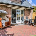 Terrace with sun lounger, table and chairs in front of a house with brick wall.