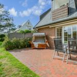 Terrace with wooden lounger and seating group in front of brick house.