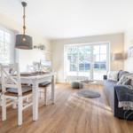 Living and dining area with wooden floor, sofa, table and chairs, and windows.