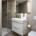 Badezimmer mit Dusche, Waschbecken und Toilette. Fliesenwand und moderne Einrichtung.