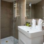 Bad mit Dusche, Waschbecken und beleuchtetem Spiegel
