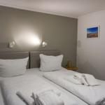 Zwei Betten mit weißen Laken und Handtüchern. Wandlampen und Bild an der Wand.