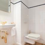 Badezimmer mit weißen Fliesen, goldenem Waschbecken und Toilette.