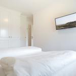 Schlafzimmer mit weißem Bett und Wandfernseher