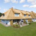 Haus mit Strohdach, Garten und Terrasse mit Sitzgelegenheiten.