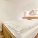 Bedroom with rattan bed, white bedding, and a white chair.