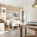 Living and dining area with sofa, dining table, and wicker chairs. Wall art and bookshelves visible.