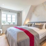 Schlafzimmer mit großem Bett, Fenster und moderner Wandgestaltung.