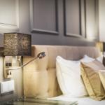 Schlafzimmer mit Beistelltisch, Wandlampe und gepolsterter Kopfseite.