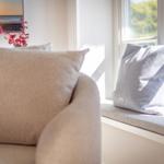 Sofa mit Kissen und Fensterbank mit Kissen und Blumen.