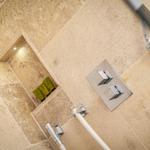 Dusche mit Steinwand, Duschbrause und integriertem Regal mit Duschgels.