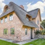Ein zweistöckiges Haus mit strohgedecktem Dach und roten Ziegelsteinen.