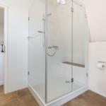 Dusche mit Glaswand, Toilette und Tür zum angrenzenden Raum.