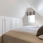 Schlafzimmer mit Dachschräge, Bett und Fenster mit Rollladen.