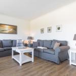 Wohnzimmer mit grauen Sofas, weißem Tisch und Holzboden.