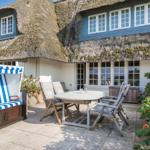 Terrace with beach chair, table and chairs in front of a house with thatched roof.