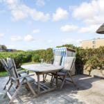 Terrace with table, chairs, and beach chairs. View of green hedge and rooftops.