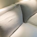 A bed with white sheets and two pillows, one of which is gray.