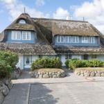 Holiday home with thatched roof and blue windows. Front garden with stone border and shrubs.