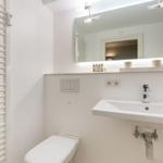 Bathroom with sink, mirror, and toilet. Warm lighting and white walls.