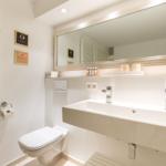 Bathroom with sink, mirror, and toilet. Warm lighting and wooden accents.