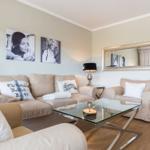 Living room with sofa, armchair, and glass table. Wall art and mirror on the walls.