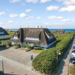 House with thatched roof, parking lot, and sea view.